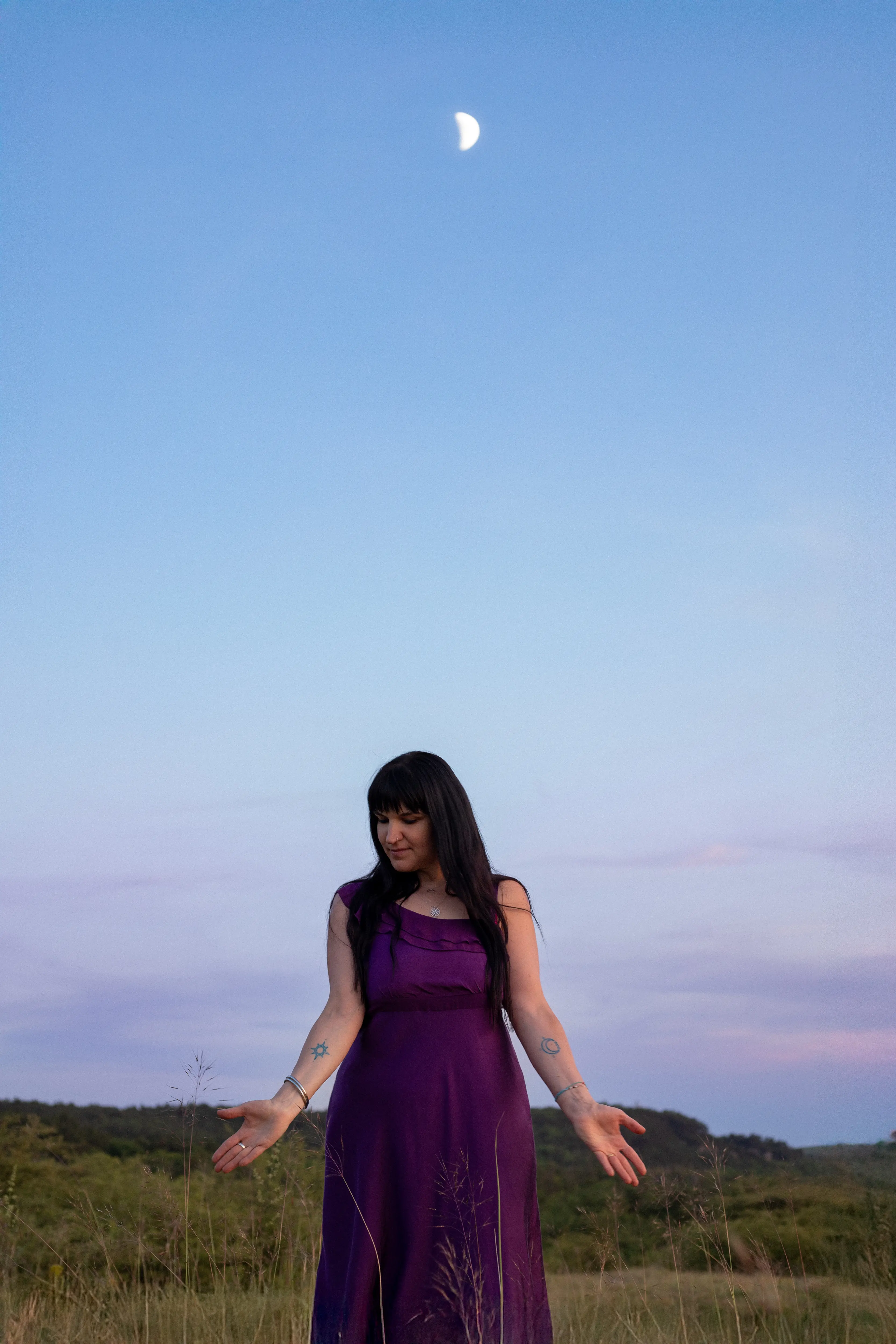 Adrienne in a purple dress at dusk beneath a crescent moon