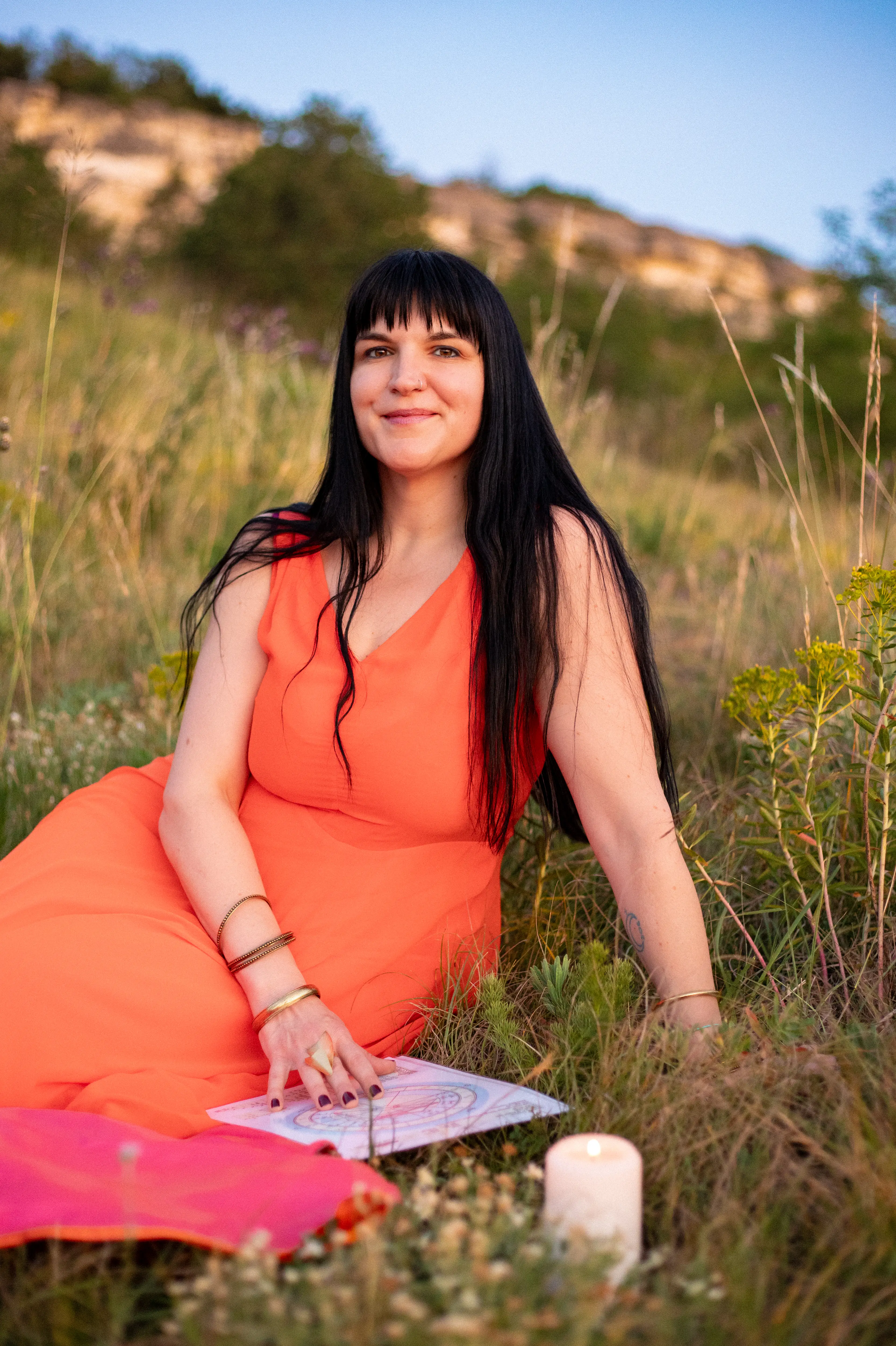 Adrienne smiling while seated in a golden field beside her natal chart and a lit candle