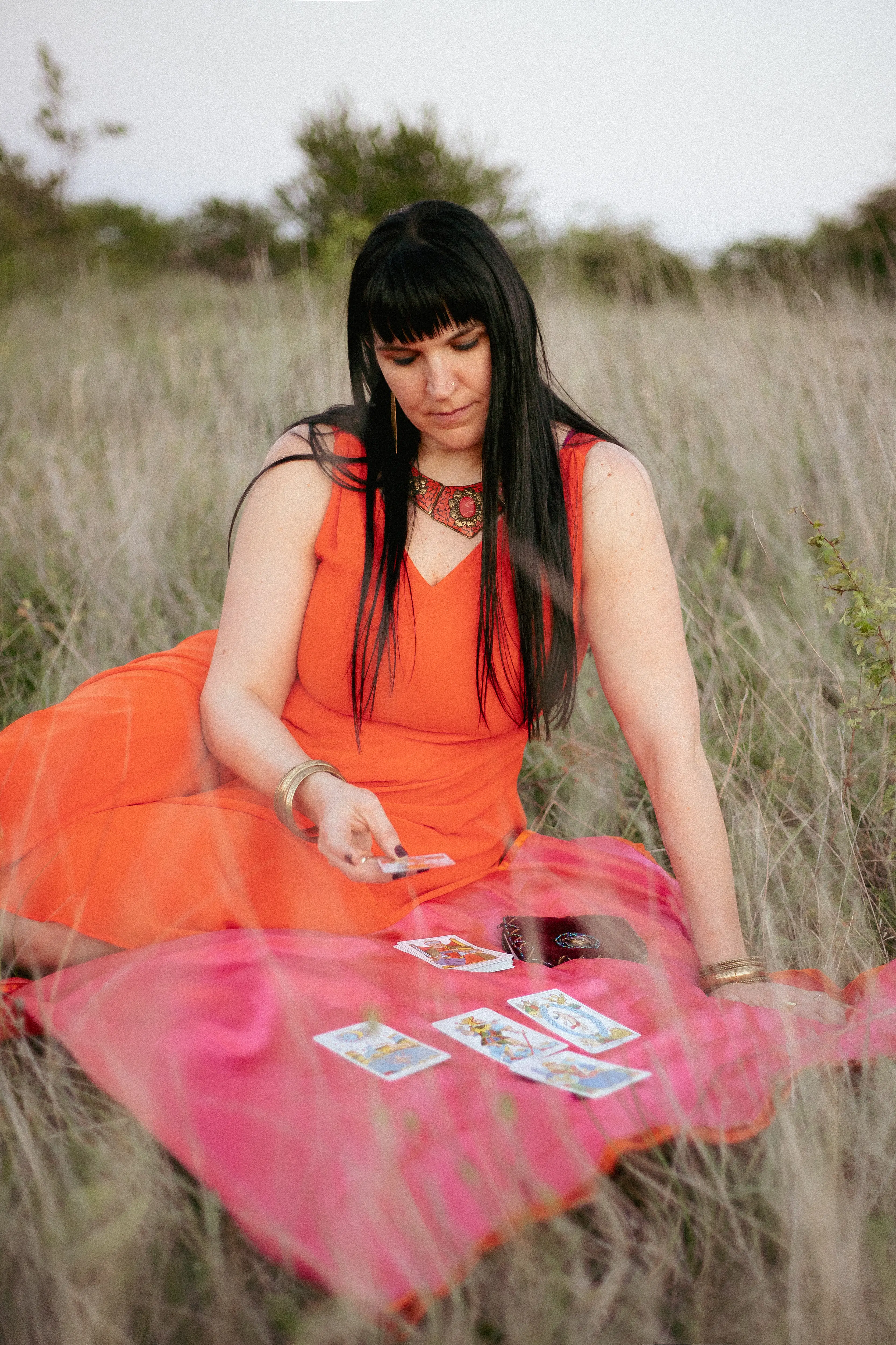 Adrienne extendiendo una baraja de tarot hacia la cámara, con tatuajes de sol y luna visibles en sus brazos